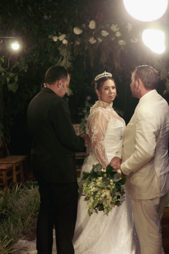 Noiva e noivo no altar com a cerimonialista ao lado durante a cerimônia de casamento