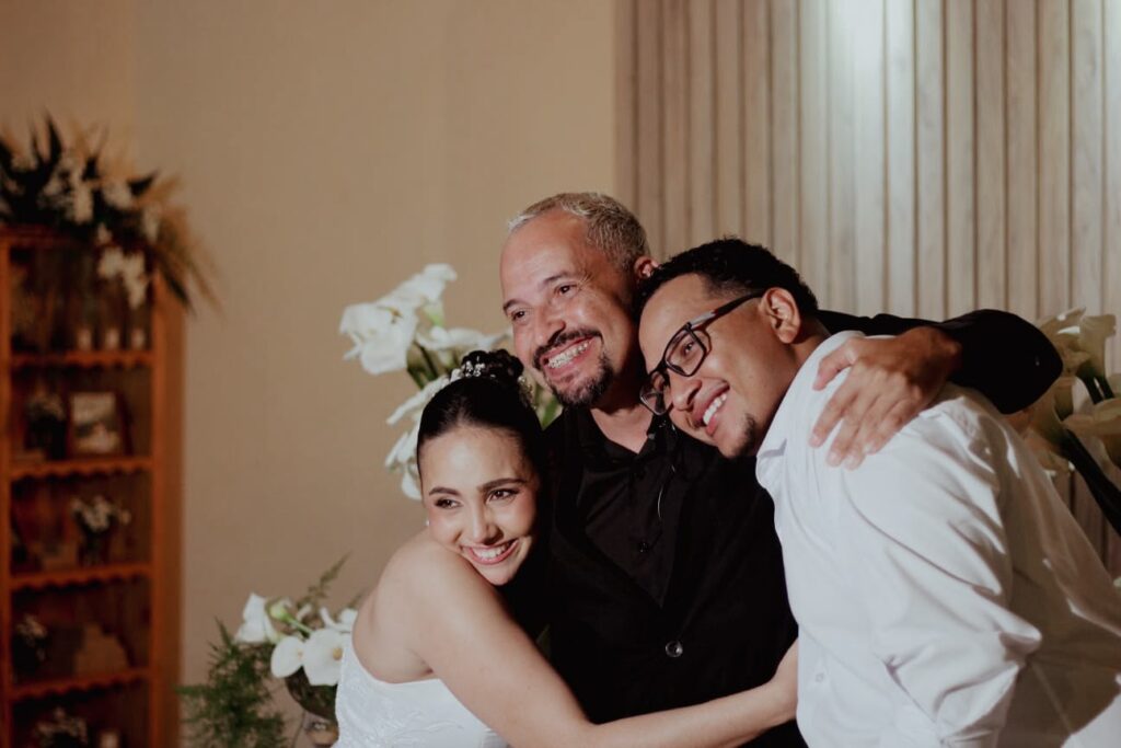 Cerimonialista abraçado aos noivos em momento de emoção após a cerimônia de casamento