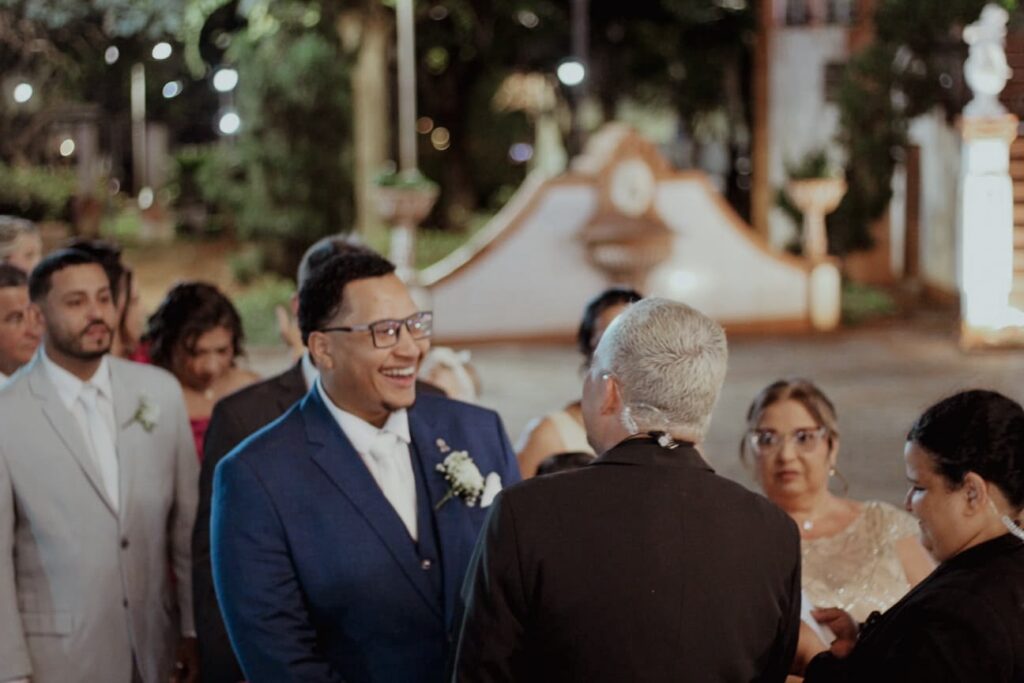 Noivo sorrindo emocionado diante do celebrante em cerimônia de casamento ao ar livre